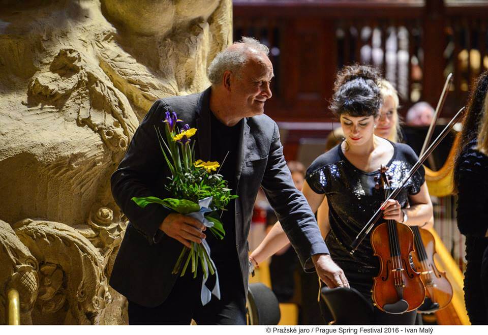 CM on stage next to a violinist, with some flowers after taking a bow