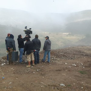 Several people standing with camera on a hill top, pointing towards a mountain view