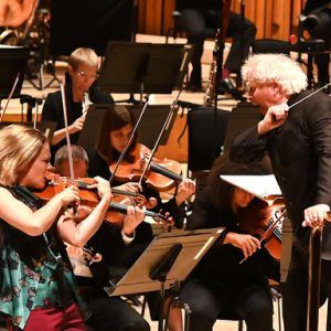 Leila Josefowicz playing the violin on stage very energetically, conducted by Simon Rattle wtih some members of the orchestra visible