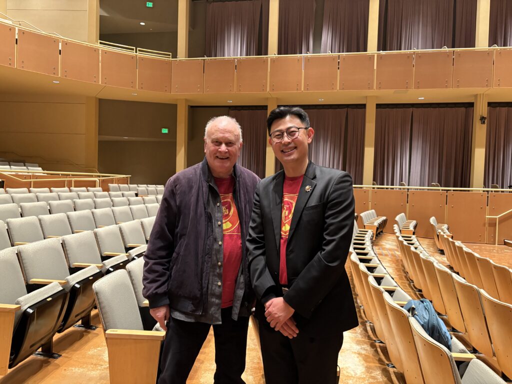 Two men pose for a photo together in an empty concert hall
