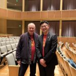 Two men pose for a photo together in an empty concert hall