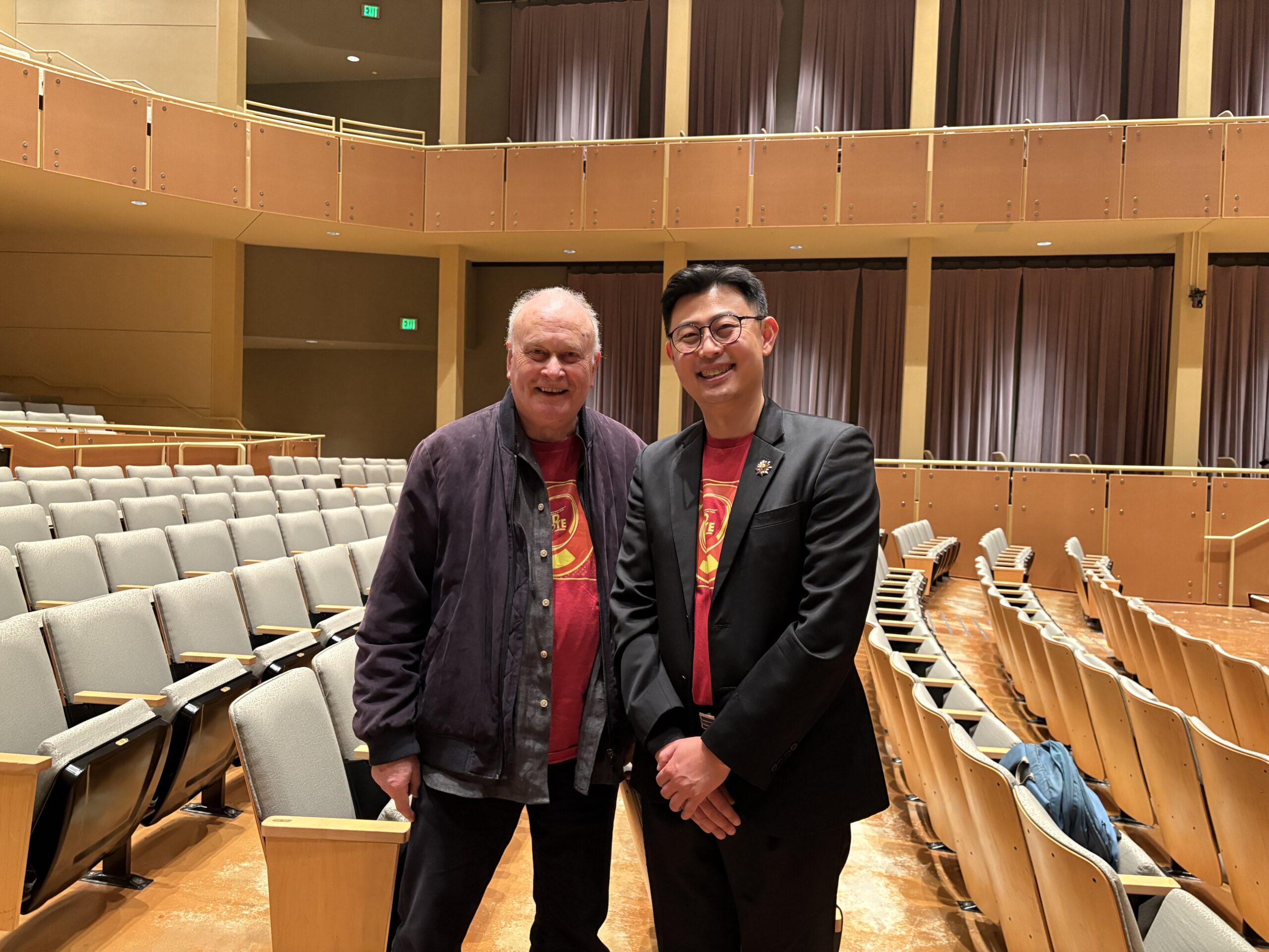 Two men pose for a photo together in an empty concert hall