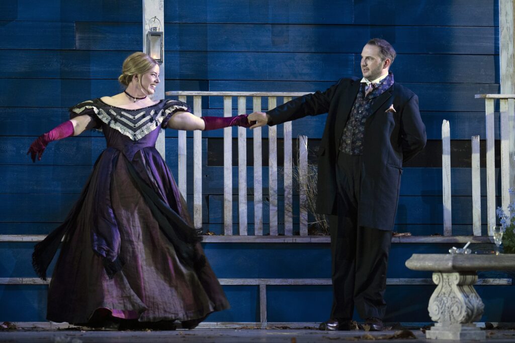 A woman and a man dressed in old-fashioned formal clothing hold hands on an opera set