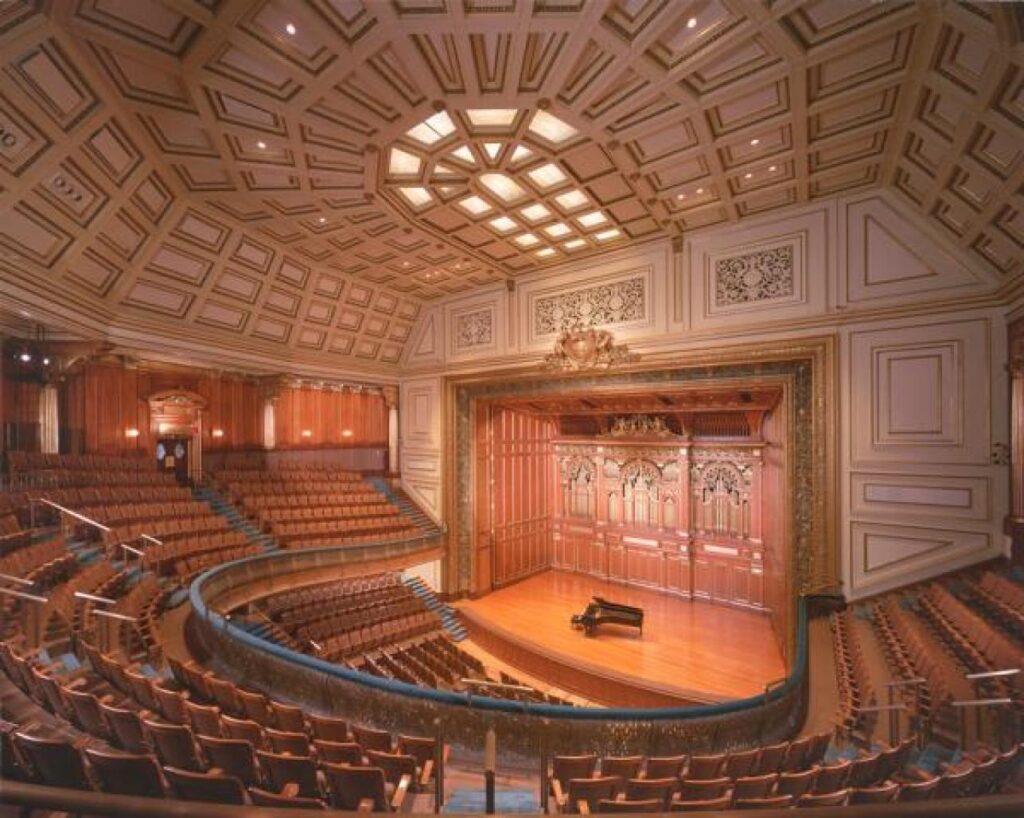 A large, empty concert hall with a grand piano on the stage