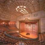 A large, empty concert hall with a grand piano on the stage