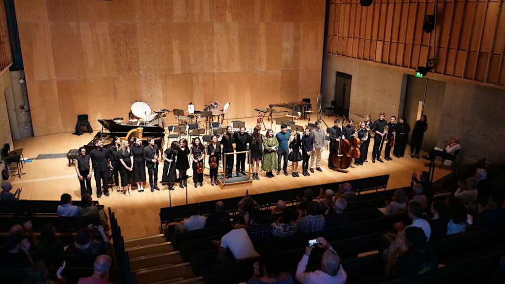 Around 25 musicians and composers line up to take a bow on stage at the Snape Maltings Concert Hall